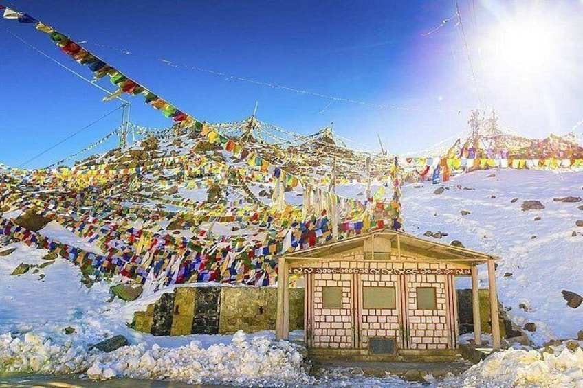 A snow-covered landscape with colorful prayer flags and a small building. 5