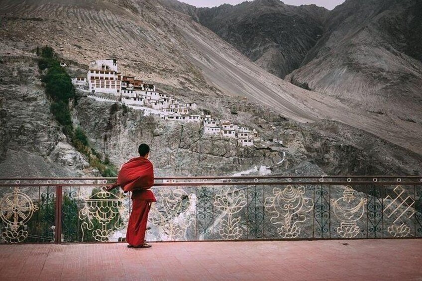 A person in red robes standing on a balcony overlooking a monastery on a mountain. 2
