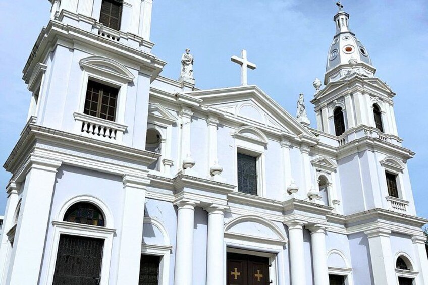 A white church with a bell tower, arched windows, and a cross on the facade. 4