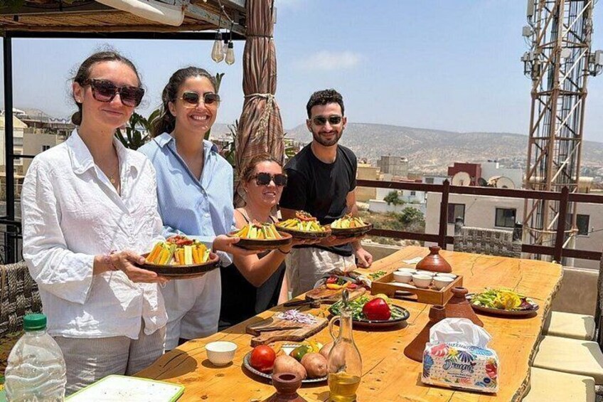 A group of people standing at a table with plates of food, a bottle of water, and a variety of dishes on the table. 1
