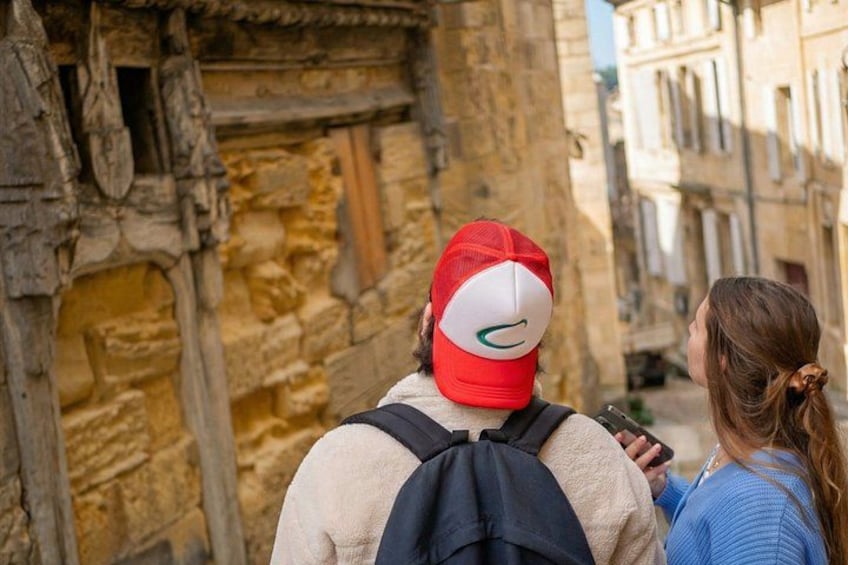 A person wearing a red cap and a beige jacket standing in front of a stone building with a narrow alleyway. 2