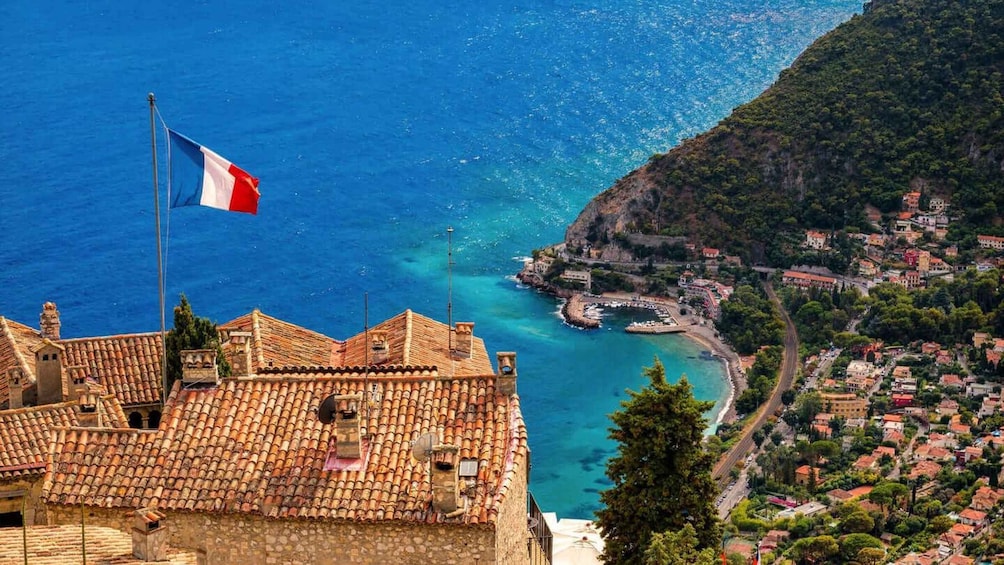 Una cittadina costiera con edifici a tetto di tegole, un mare cristallino e una bandiera su un'asta. 1