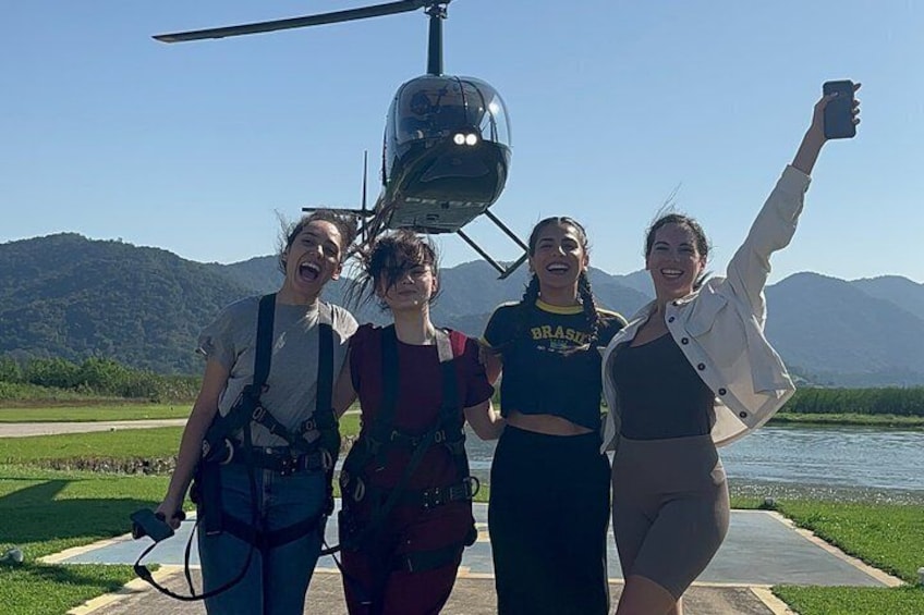 Four people standing in front of a helicopter with a lake and mountains in the background. 4