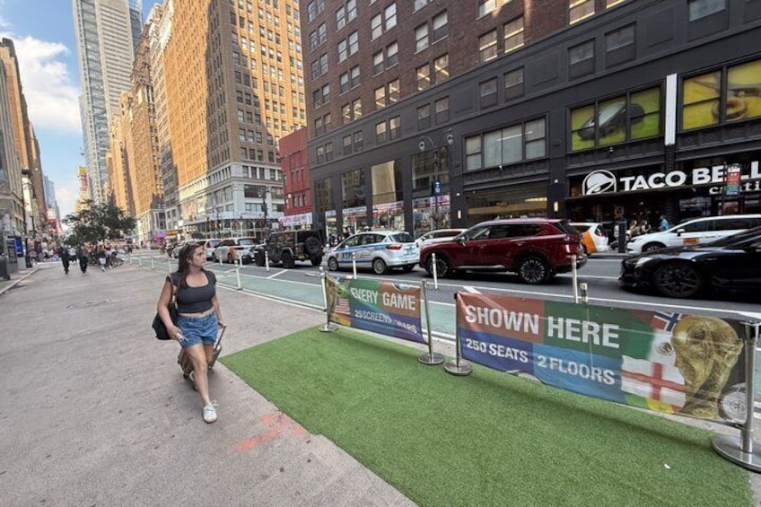 A city street with a green artificial turf area, a Taco Bell restaurant, and a sign advertising a game. 2
