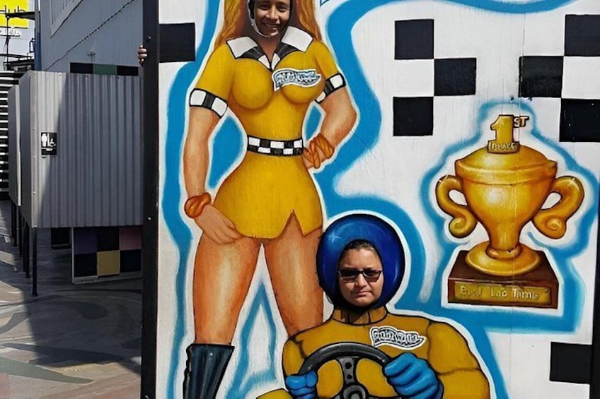 A mural with a woman in a yellow outfit and a man in a yellow shirt holding a steering wheel, with a trophy in the background. 2