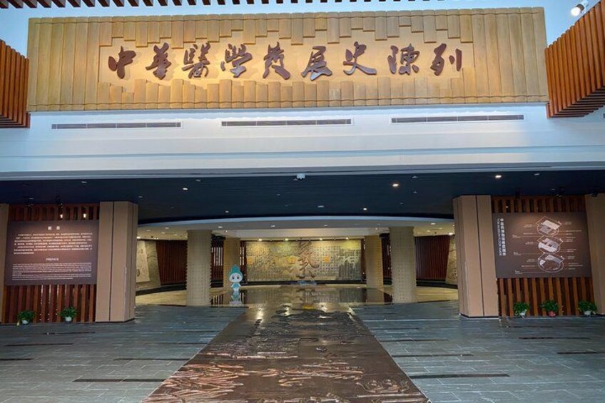A modern building entrance with a large sign, a wet floor, and decorative plants. 2