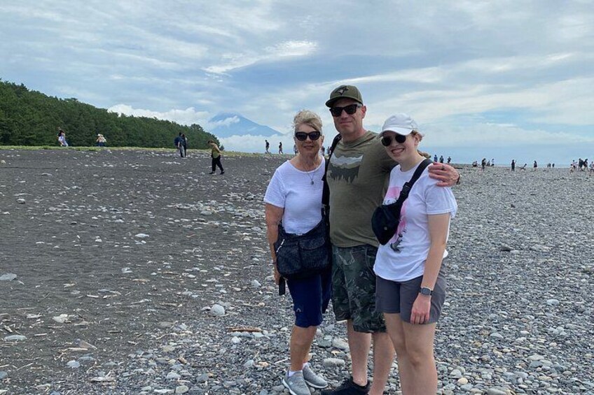 A rocky beach with people walking, a mountain in the background, and a cloudy sky. 2