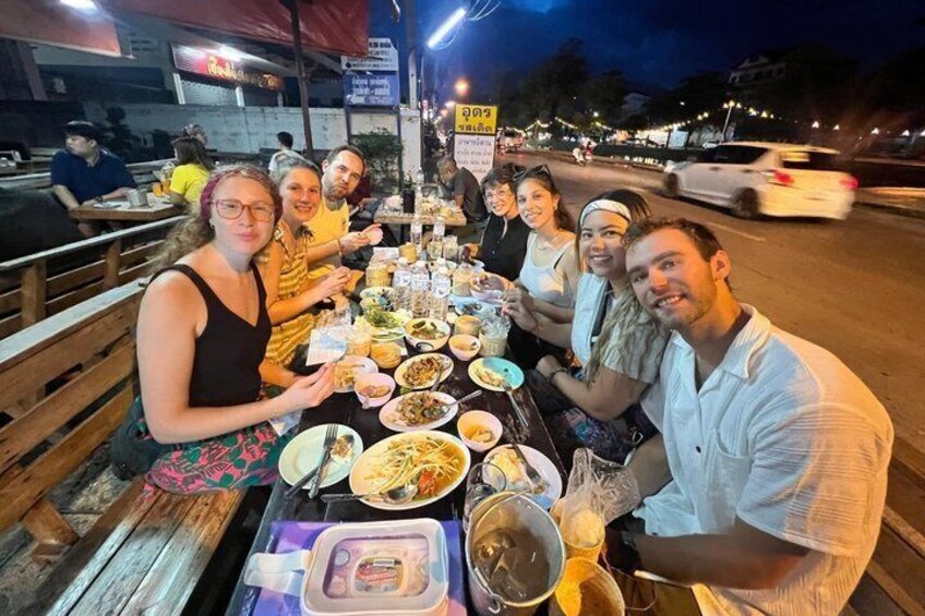 A group of people dining at an outdoor restaurant with various dishes on the table. 1