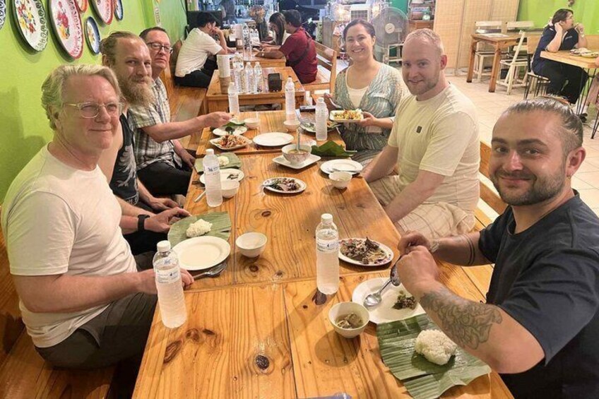 A group of people dining at a wooden table in a restaurant with plates of food and water bottles. 5