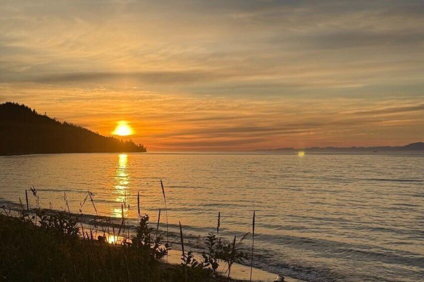 A sunset over a calm body of water with a distant shoreline and a fence in the foreground. 2