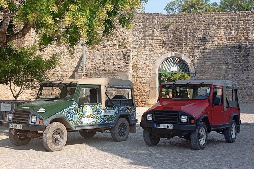 Two off-road vehicles parked in front of a stone wall with an arched doorway. 3