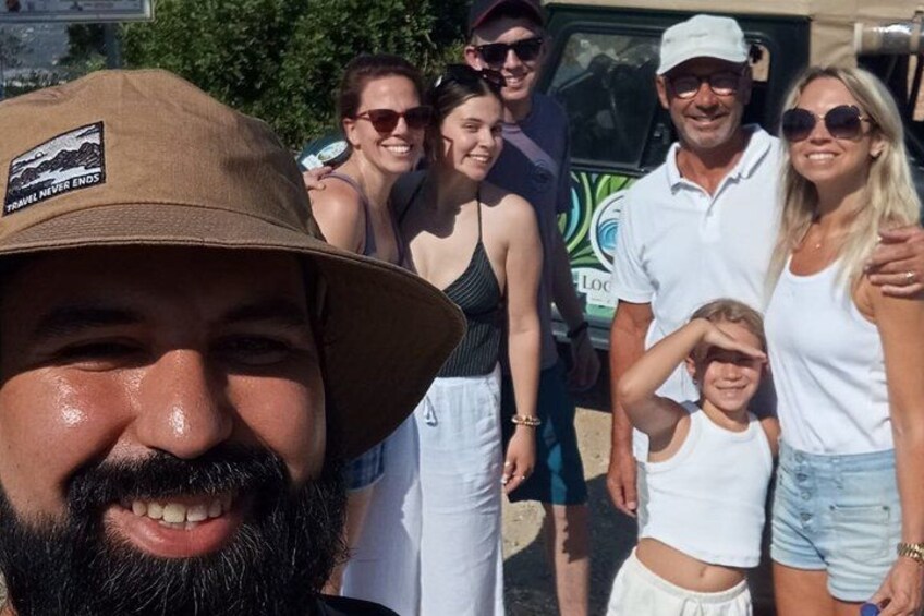 A group of people standing outdoors, some wearing hats and sunglasses, with a vehicle in the background. 5