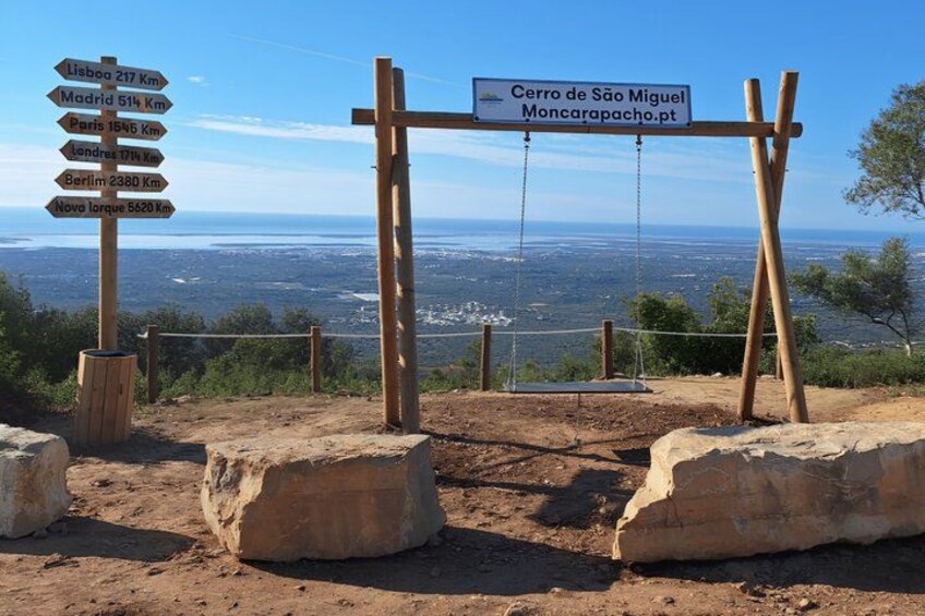 A signpost with distance markers to various cities, a wooden swing, and a view of the landscape. 5