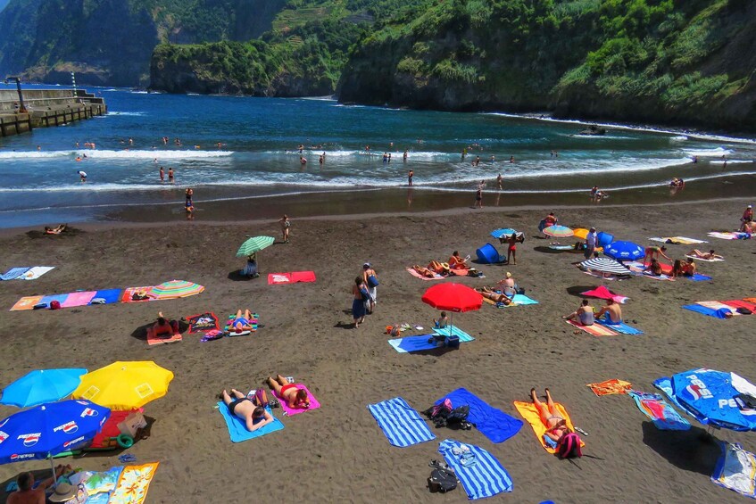 A beach with people sunbathing and swimming, surrounded by cliffs and a pier. 4