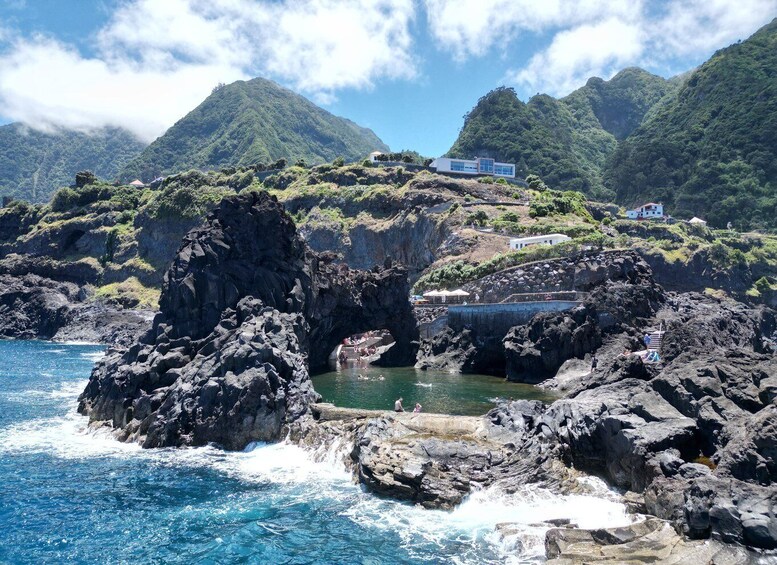 A coastal landscape with rocky cliffs, a clear blue sea, and buildings perched on the hillside. 3