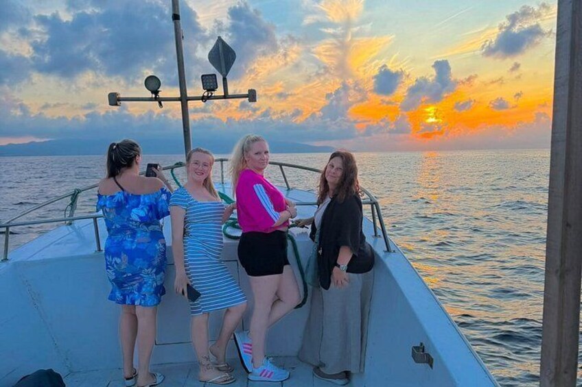 A boat with four people on a calm sea during sunset. 4