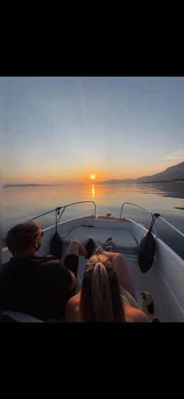 A boat with two people facing the sunset over calm water. 2