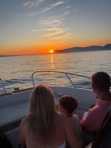 A boat with three people at sunset, facing the ocean. 1