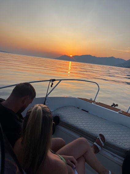 A boat with two people on deck, a sunset, calm water, and mountains in the background. 3