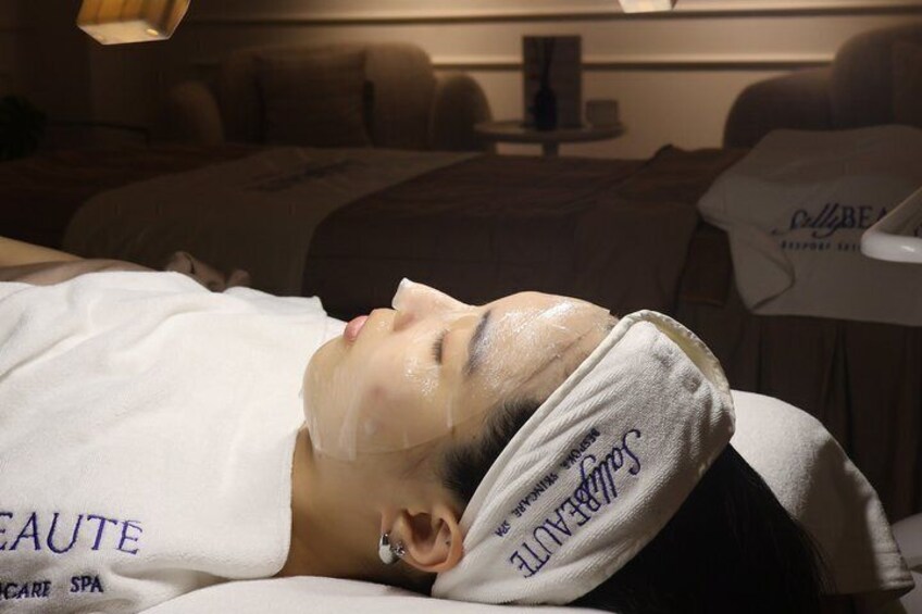A person lying on a bed with a towel over their head, in a room with a massage chair and a white wall with text. 3