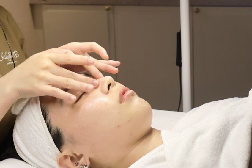 A person lying down with a towel on their head, receiving a facial treatment. 4
