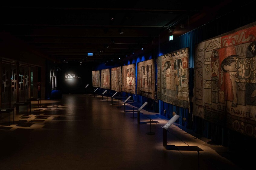 A dimly lit museum corridor with ancient wall paintings and a blue curtain at the end. 2