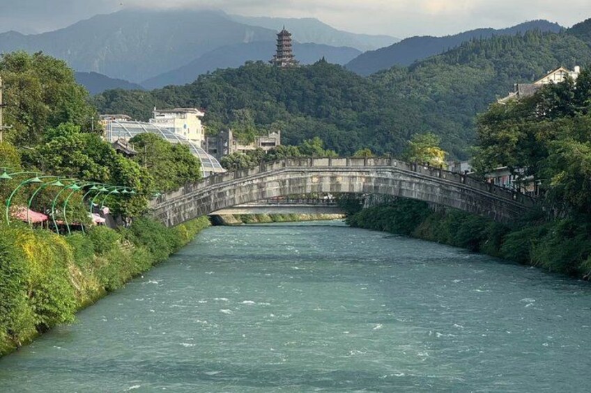 A river with a stone bridge, lush greenery, and a pagoda in the background. 4