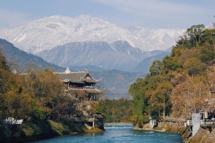 A traditional building by a river with mountains in the background. 2