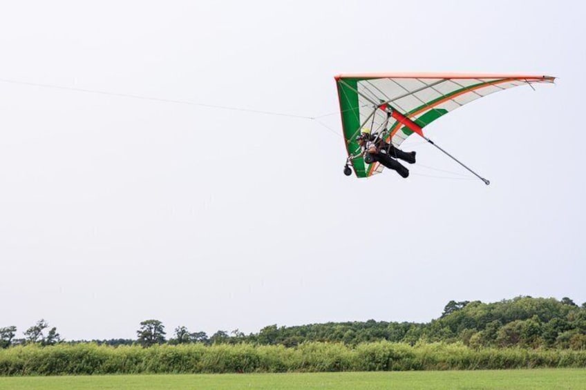 A paraglider in mid-flight over a grassy field with trees in the background. 3