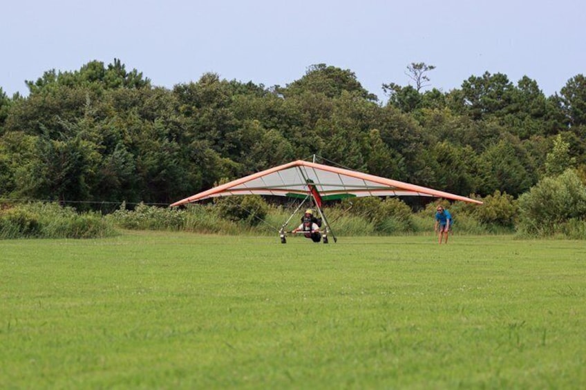 A glider with a red and white canopy on a grassy field with a forest in the background. 4
