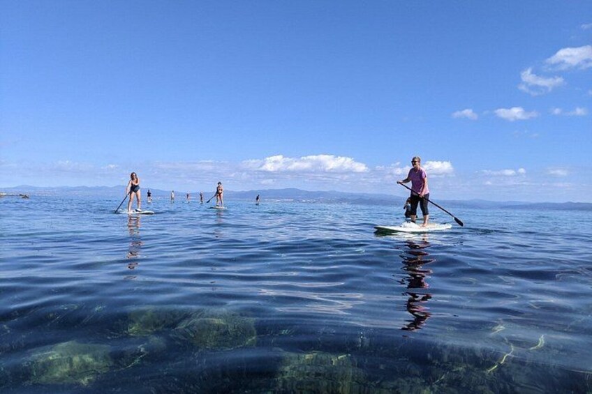 People paddleboarding on a calm sea with clear water and a clear sky. 3