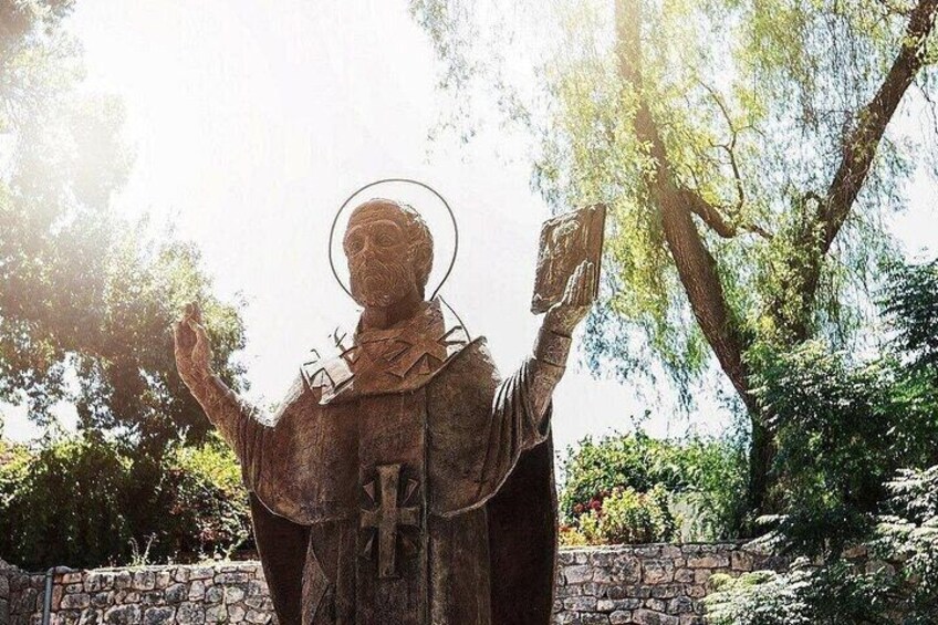 A statue of a person in a robe holding a book and a tablet, set against a stone wall and trees. 5