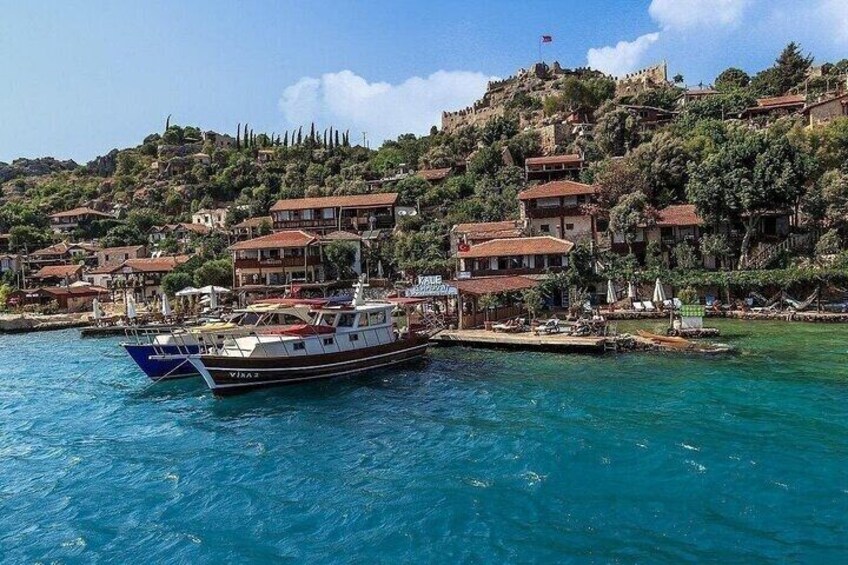 A boat named 'VINA' docked at a harbor with buildings on a hillside in the background. 3