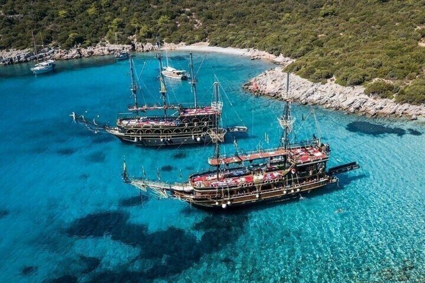 A clear blue sea with three large boats anchored near a rocky shore. 2