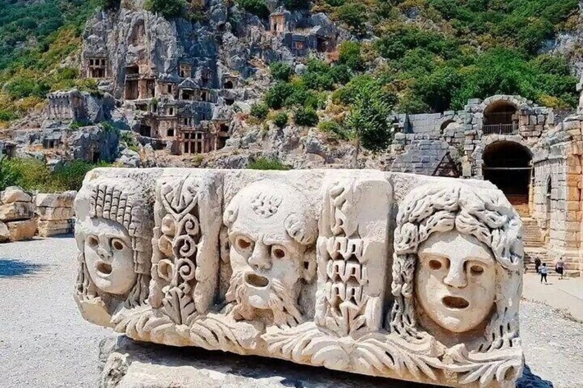 A stone relief with carved faces and a mountainous backdrop. 1
