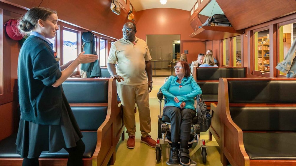 A train interior with wooden paneling, blue seating, and a wheelchair. 1