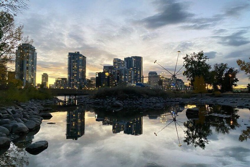 A city skyline reflected in a calm body of water with rocks and trees in the foreground. 3