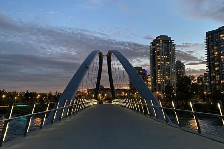 A modern bridge with two large arches, a river below, and city buildings in the background. 2