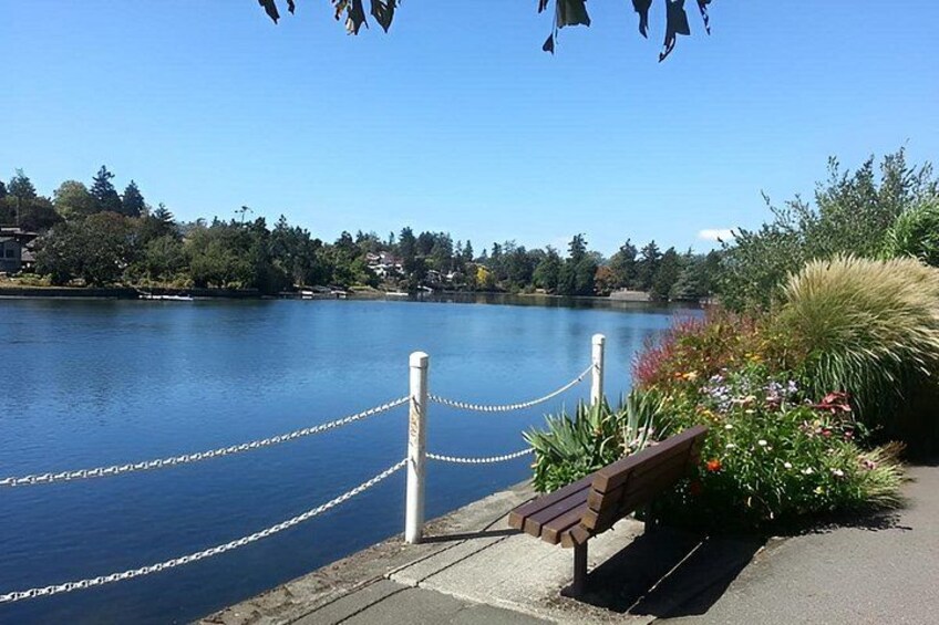 A lakeside walkway with a wooden bench, a rope barrier, and lush greenery. 3
