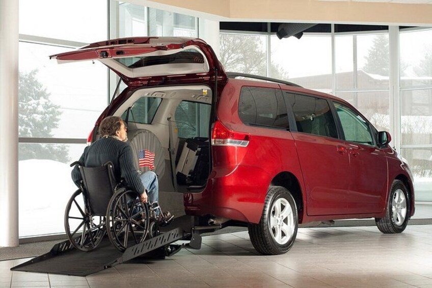 A red minivan with its rear door open, a person in a wheelchair, and a ramp leading into the vehicle. 2
