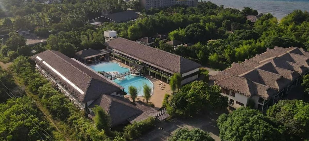 A resort with a swimming pool, surrounded by lush greenery and buildings with thatched roofs. 2