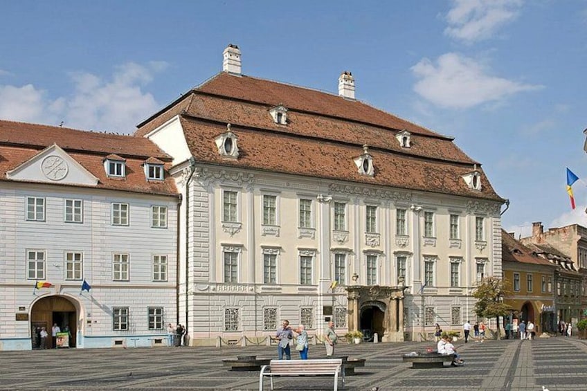 A historic building with a red roof and white facade, surrounded by a plaza with benches and people. 4