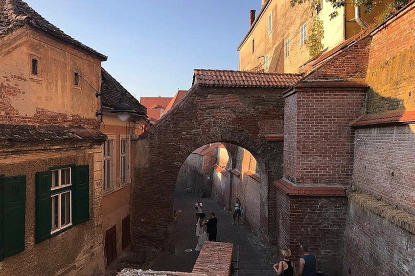 A narrow alleyway with a brick archway, old buildings, and a clear sky. 5