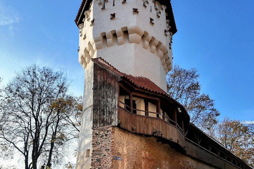 A historic tower with a brick base and white upper section, featuring a wooden balcony. 2