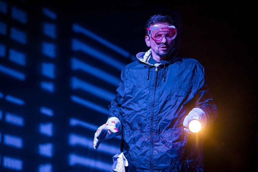 A person in a dark jacket with a hood, holding a light source. 5