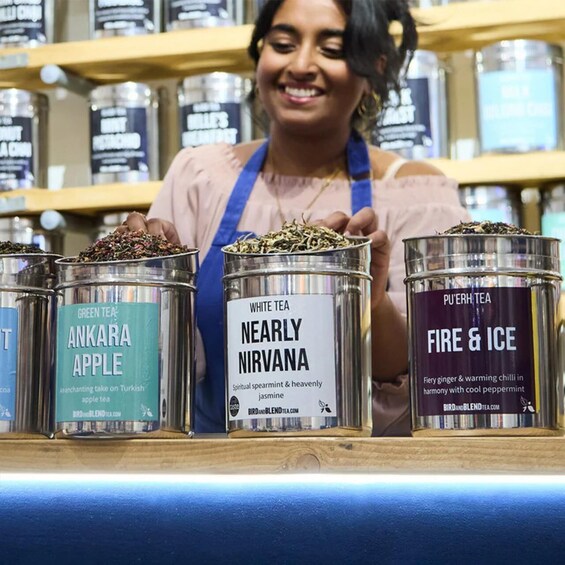 A person behind a counter with tea containers labeled 'Green Tea Ankara Apple,' 'White Tea Nearly Nirvana,' and 'Pu'erh Tea Fire & Ice.' 1