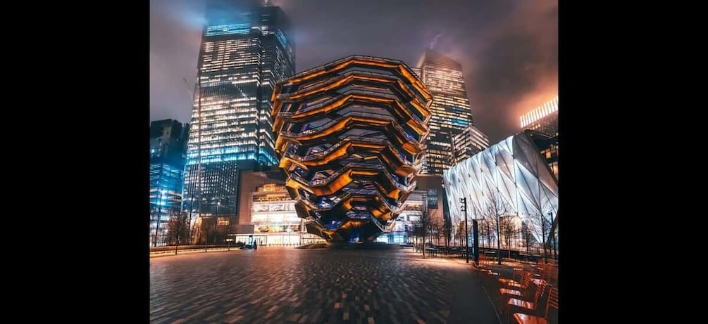 A cityscape with a prominent hexagonal building in the center, surrounded by high-rise buildings with illuminated windows. 3