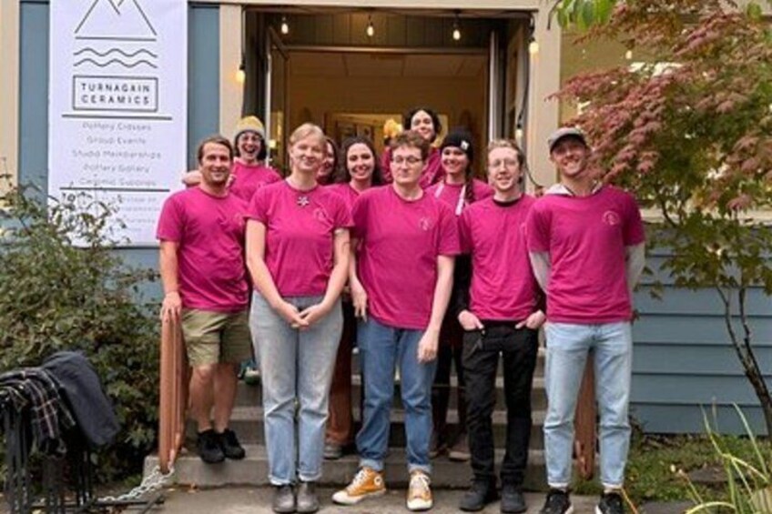 A group of people in pink shirts standing in front of a building with a sign that reads 'Turnagain Ceramics.' 4