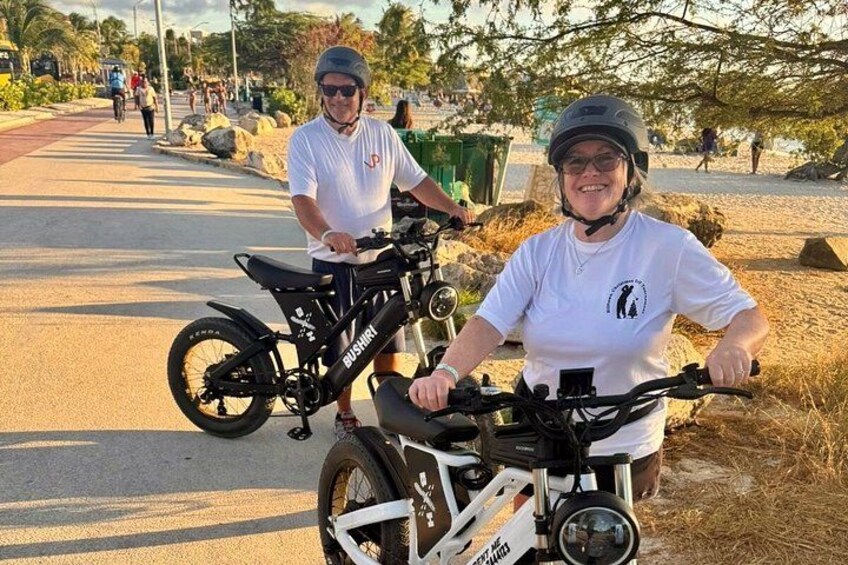 Two people on bicycles on a paved path with trees and rocks in the background. 4