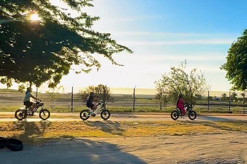 Three people riding bicycles on a dirt path with trees and a fence in the background. 5